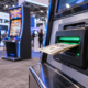 Editorial illustration of casino bill validator technology, a gaming machine, and a trade-show floor